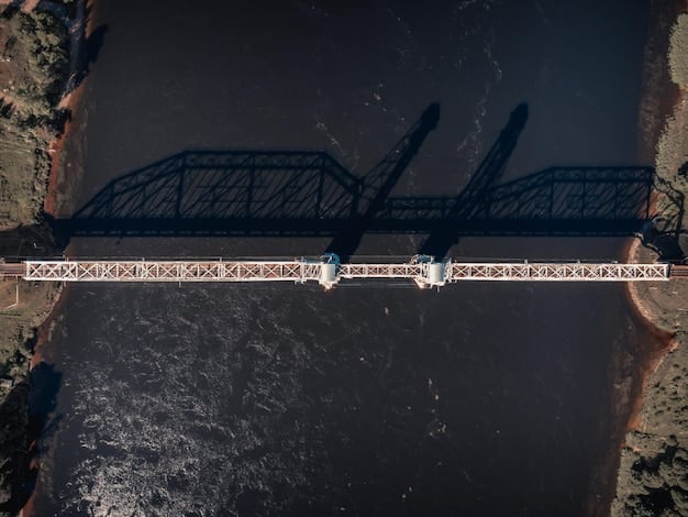 An aerial view of a large-scale bridge construction project in a major US city. Cranes and construction equipment are actively moving, and workers can be seen on the bridge structure. The surrounding landscape includes a river and cityscape, emphasizing the project's scale and integration within the urban environment.