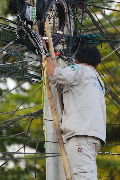 A close-up shot of a technician installing fiber optic cables in a rural area. The technician is wearing safety gear, and the surrounding environment shows open fields and a few houses in the distance, highlighting the expansion of internet access to underserved communities.