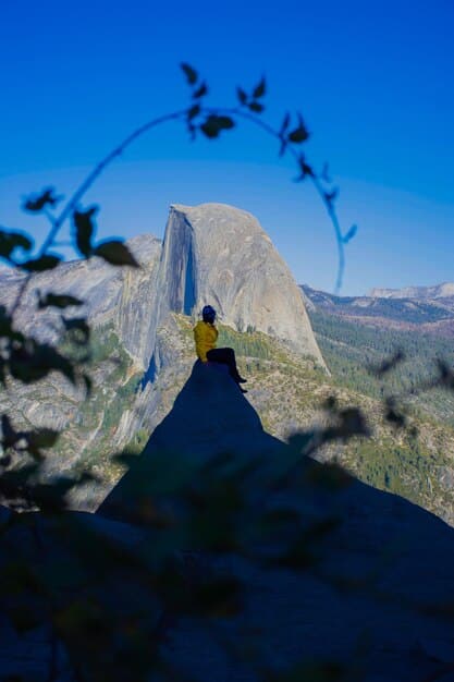 A wide shot of Alex Honnold free soloing a section of El Capitan, emphasizing the vastness of the rock face and the sheer drop below him.